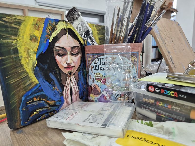 Close-up of a student painting on a large colorful canvas at a Royal Blue studio, showing hands with a brush applying paint to a vibrant figurative artwork