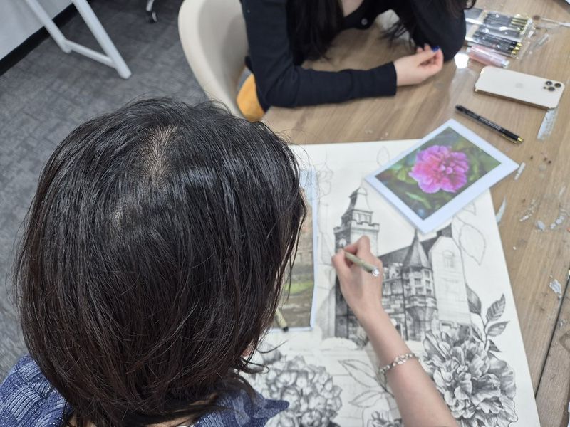 Photograph of an instructor or student working closely on a large dark dramatic artwork at a Royal Blue studio, adding fine details with a brush surrounded by reference images