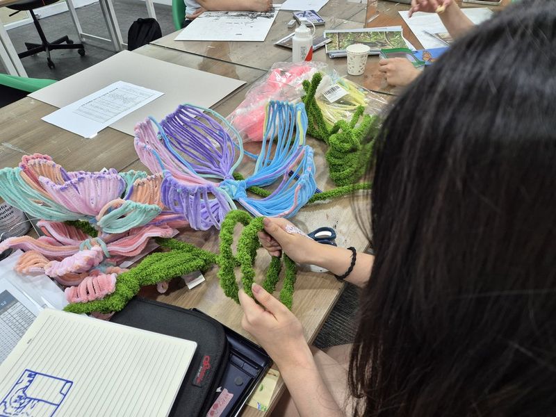 Royal Blue branded photograph of a student working on a floral or botanical still life drawing or painting at a studio table, with flowers and art supplies visible nearby