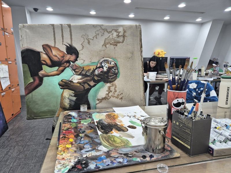 Photograph of an instructor or senior student demonstrating painting techniques on a large colorful canvas in a Royal Blue studio, surrounded by reference artworks