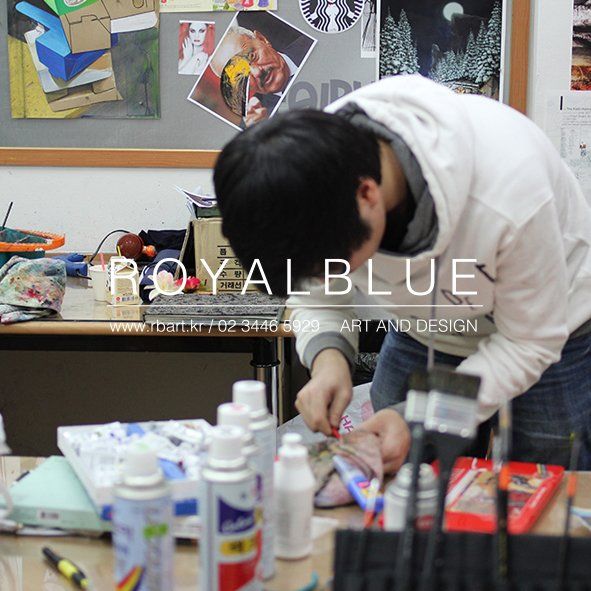 Royal Blue branded photograph of a Royal Blue studio workspace showing art supplies, reference images, and bottles of paint or medium arranged on a desk for a class session
