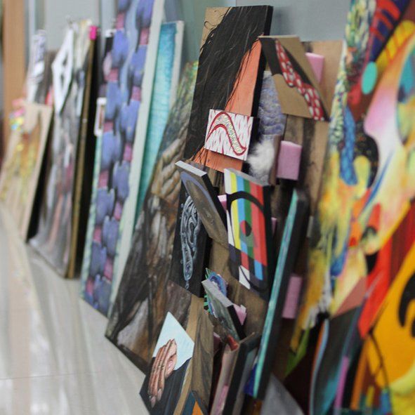 Royal Blue branded photograph of a student working on a large colorful mixed-media artwork at a Royal Blue studio, surrounded by multiple artworks and reference materials pinned to walls