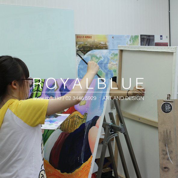 Royal Blue branded photograph of a student working on a large canvas mounted on an easel, applying paint with broad brushstrokes to a colorful artwork in a Royal Blue studio