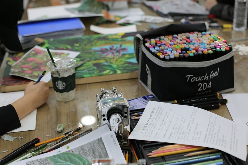 Photograph of a student at a Royal Blue studio looking at reference materials and working on an illustration with Copic markers and colored media at a desk