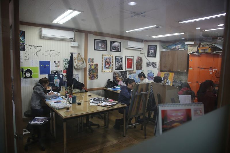 Wide interior photograph of a Royal Blue studio showing multiple students working at desks in a room with orange walls and colorful artwork displayed throughout the space
