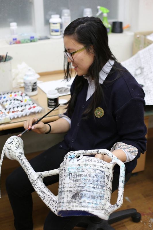 Photograph of a student at a Royal Blue studio working on a laptop computer with art references visible on screen, alongside drawing materials on the desk