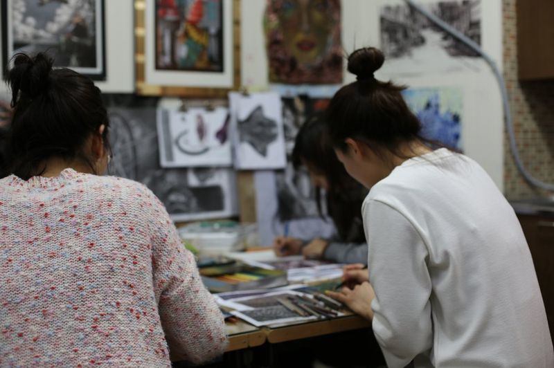 Wide photograph of a Royal Blue studio showing multiple students working at tables with artworks pinned on the walls, in a studio environment full of creative work in progress