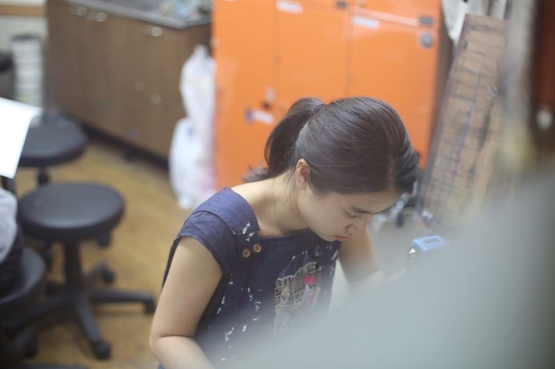 Photograph of a student at a Royal Blue studio leaning closely over a work surface and looking intently at a digital reference or device while working on an art project