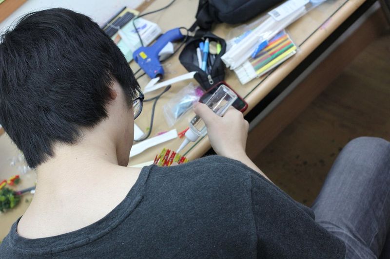 Photograph of a student at a Royal Blue studio viewed from behind, working on a detailed drawing or illustration at a desk with reference images and art supplies around them