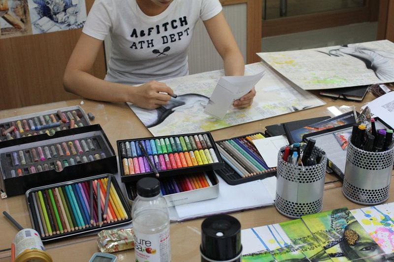 Overhead photograph of a Royal Blue studio desk showing an organized array of pastel sticks, colored pencils, and art supplies arranged for a class session