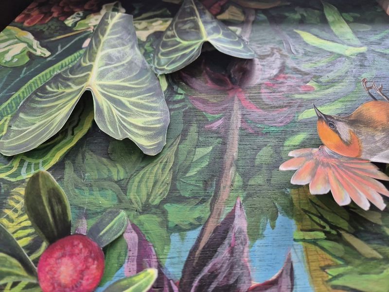 Photograph of a large detailed painting in a Royal Blue studio featuring an elaborate floral and nature composition with a central figurative element, rendered in warm tropical colors