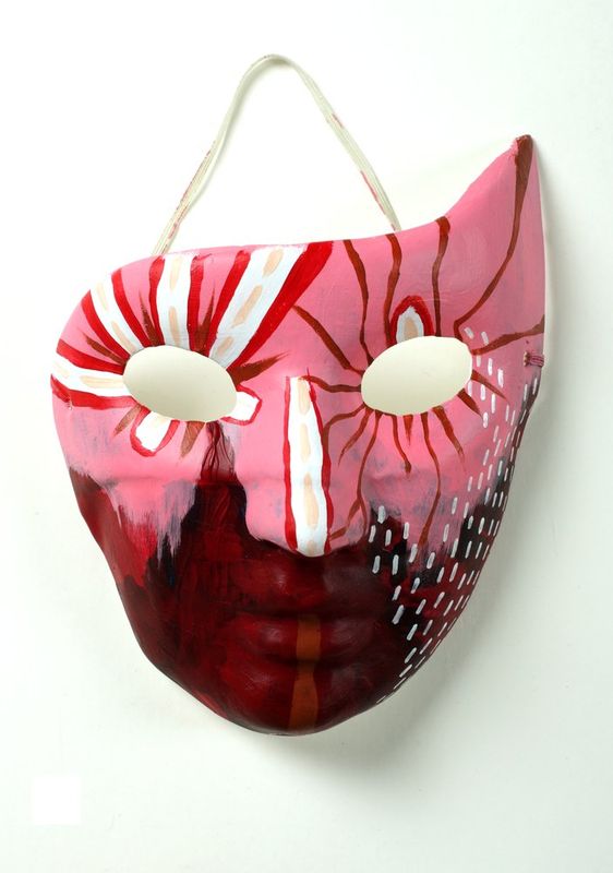 Photograph of a hand-painted decorative mask in pink and red tones with dramatic mouth and eye features, photographed against a white background as a student ceramic or painted art piece