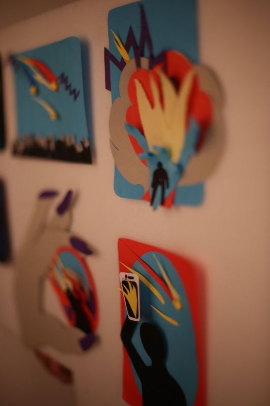 Photograph of a Royal Blue studio wall or corner showing several colorful small painted artworks featuring hands or abstract forms, displayed at an angle against an orange-toned wall