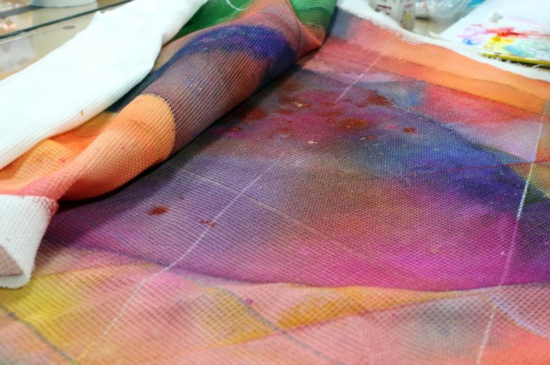 Close-up photograph of colorful translucent organza or silk fabric pieces in pink, purple, and orange tones, capturing the texture and layered quality of art materials for a fashion or textile project