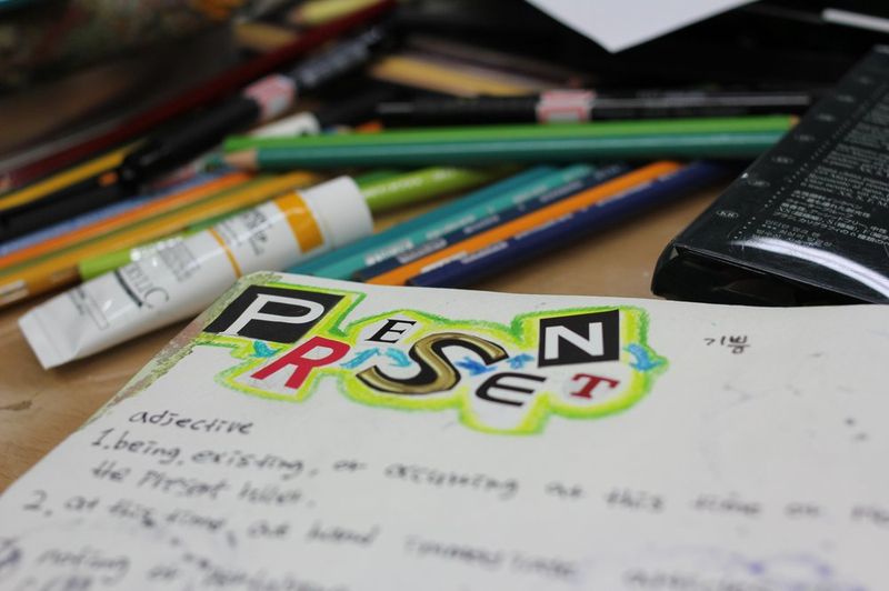 Overhead close-up photograph of a Royal Blue studio desk surface showing colored pencils, sketchbooks, and a partially complete illustration with bold lettering and colorful design work