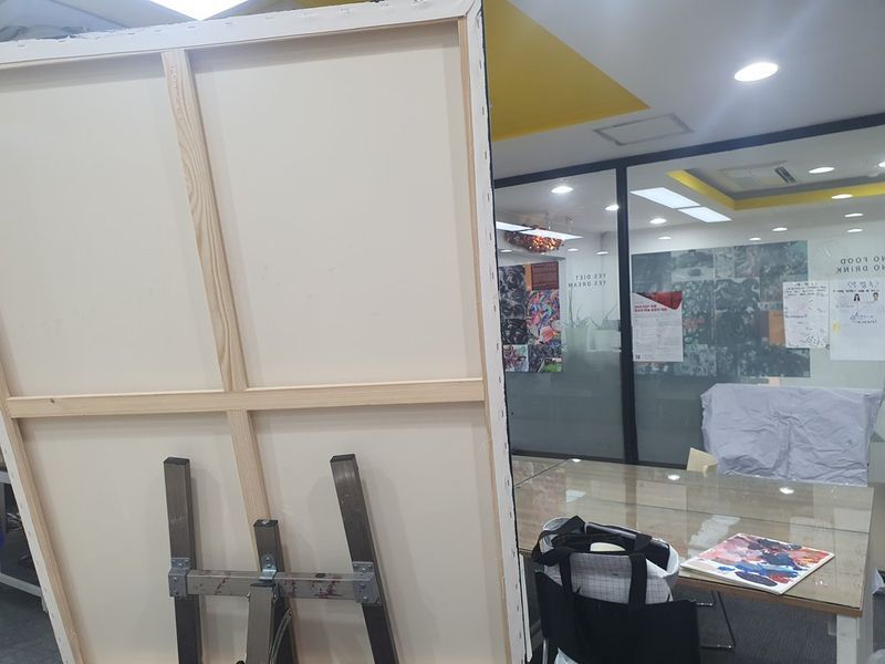 Interior photograph of a bright art studio space with white partitioned walls, yellow ceiling panels, and open working area with natural and artificial lighting