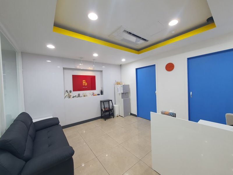 Interior photograph of a compact art studio lounge area with dark sofas, blue accent wall, and decorative artwork, showing a comfortable student relaxation space