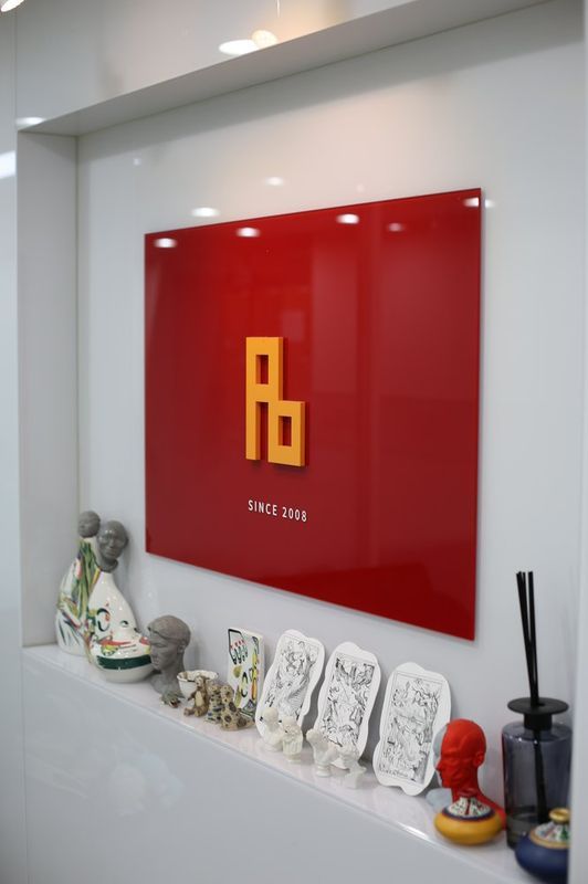 Interior photograph of the Royal Blue studio showing a red wall with the gold Rb logo, student artwork displayed on a shelf, and art supplies arranged on a white table