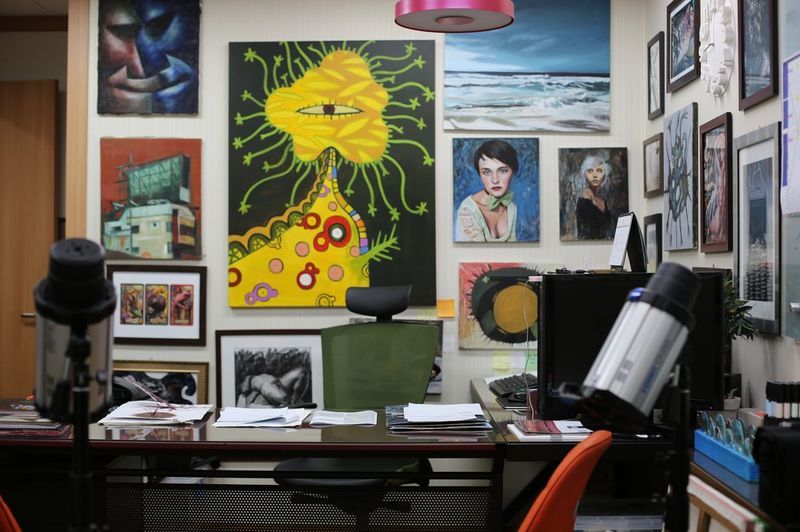 Interior photograph of a Royal Blue studio display wall covered with various framed artworks, paintings, and drawings, with studio equipment and a monitor visible in the foreground