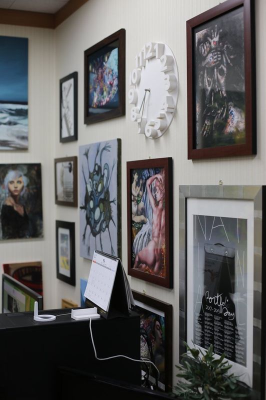 Interior photograph of a Royal Blue studio display wall densely covered with framed student drawings, prints, and mixed-media works in a salon-style hanging arrangement