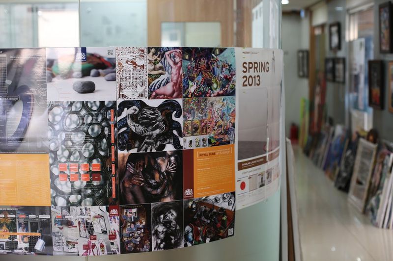 Interior photograph of a Royal Blue studio exhibition or event space showing a wall covered with colorful posters, brochures, and promotional materials alongside displayed artworks