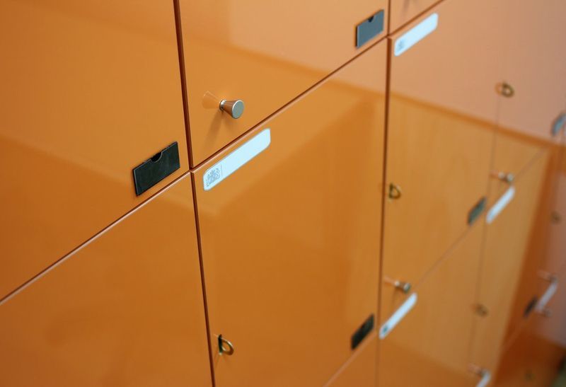 Close-up photograph of orange modular storage lockers with metal handles, showing a row of personal storage units in a studio facility for student use
