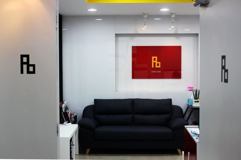 Interior photograph of a Royal Blue studio waiting or lobby area featuring the red Rb branded wall panel, black sofa seating, and clean modern interior design