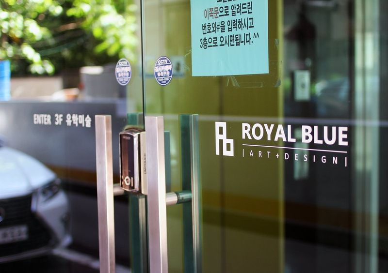 Exterior or interior photograph of the Royal Blue studio glass entrance showing the Rb logo and full studio name printed on the glass surface with the interior visible beyond