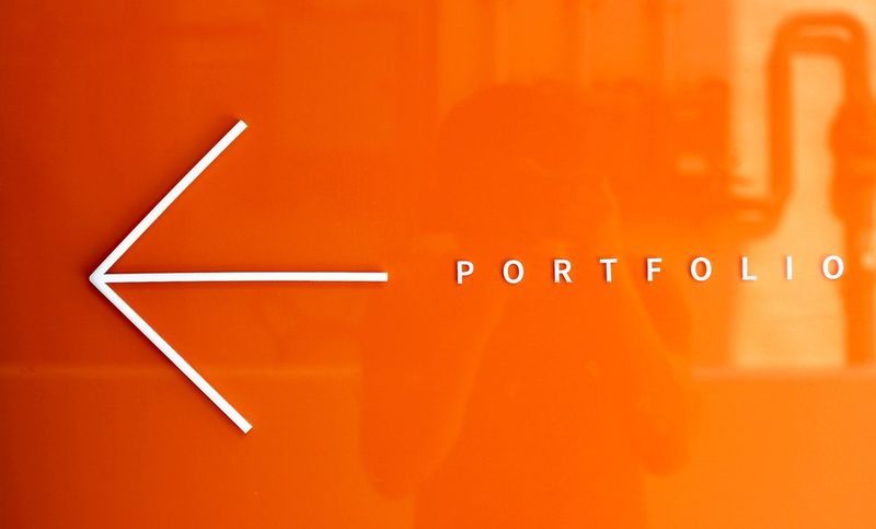 Promotional graphic design for Royal Blue showing an orange background with a large white left-pointing arrow and the word PORTFOLIO in bold white letters, used as directional or marketing signage