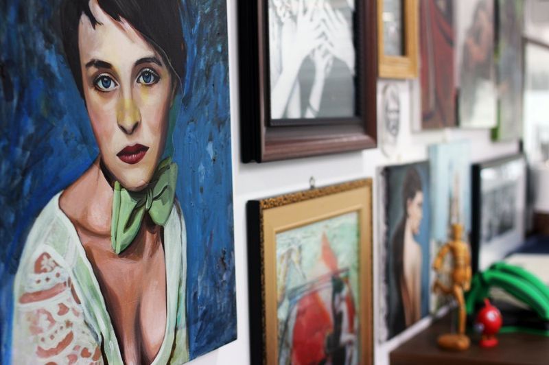 Interior photograph of a Royal Blue studio wall displaying large colorful paintings including a prominent portrait, with decorative objects and framed artworks arranged in a gallery-style setting