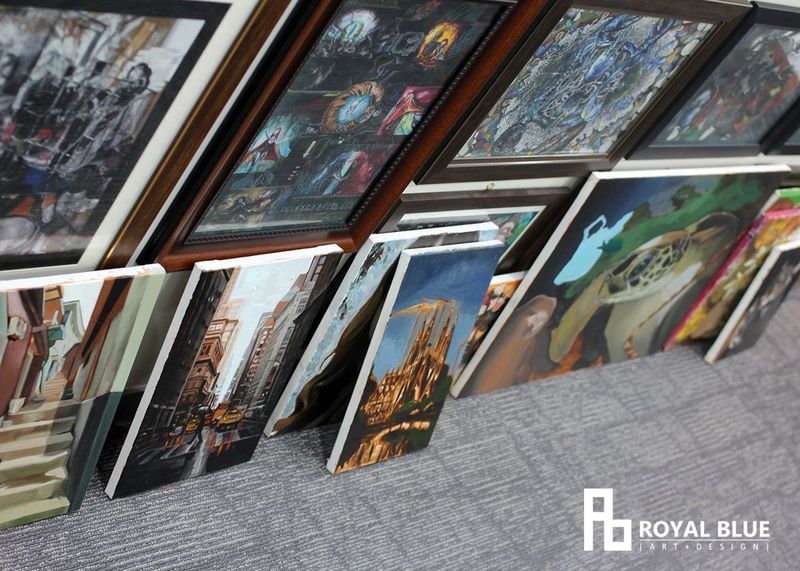 Interior photograph of a hallway or staircase wall in a Royal Blue studio building lined with numerous framed artworks, with the Royal Blue logo visible and artworks densely covering the surface