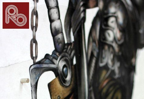 Close-up photograph of a sculptural or architectural detail featuring ornate metalwork or decorative relief with the Royal Blue Rb logo embedded within the intricate design